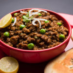 Indian Masala Kheema Pav or khima or Dry Spicy Minced Meat usually served with indian flat bread called kulcha/roti/chapati, garnished with green peas. Selective focus