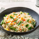 Dark grey plate with hot fried long rice and vegetables, green beans, carrot, bell pepper.